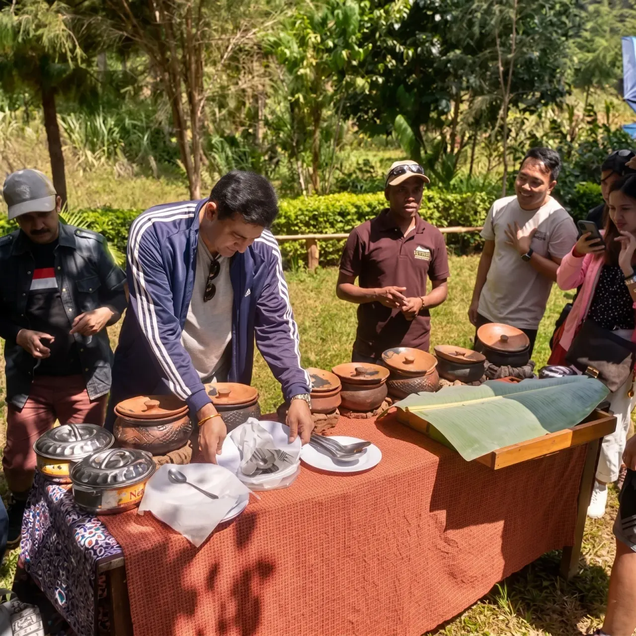 Visitors gathered around a table of clay cooking pots at a Magamba village cultural tour, a guide laying out fresh ingredients