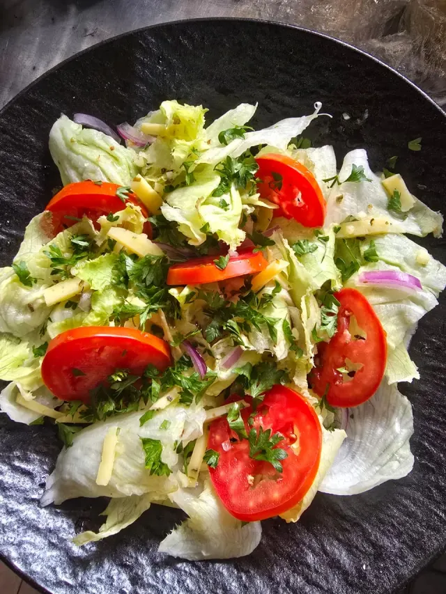 A fresh garden salad of crisp lettuce, tomato, and herbs on a dark plate at Mullers