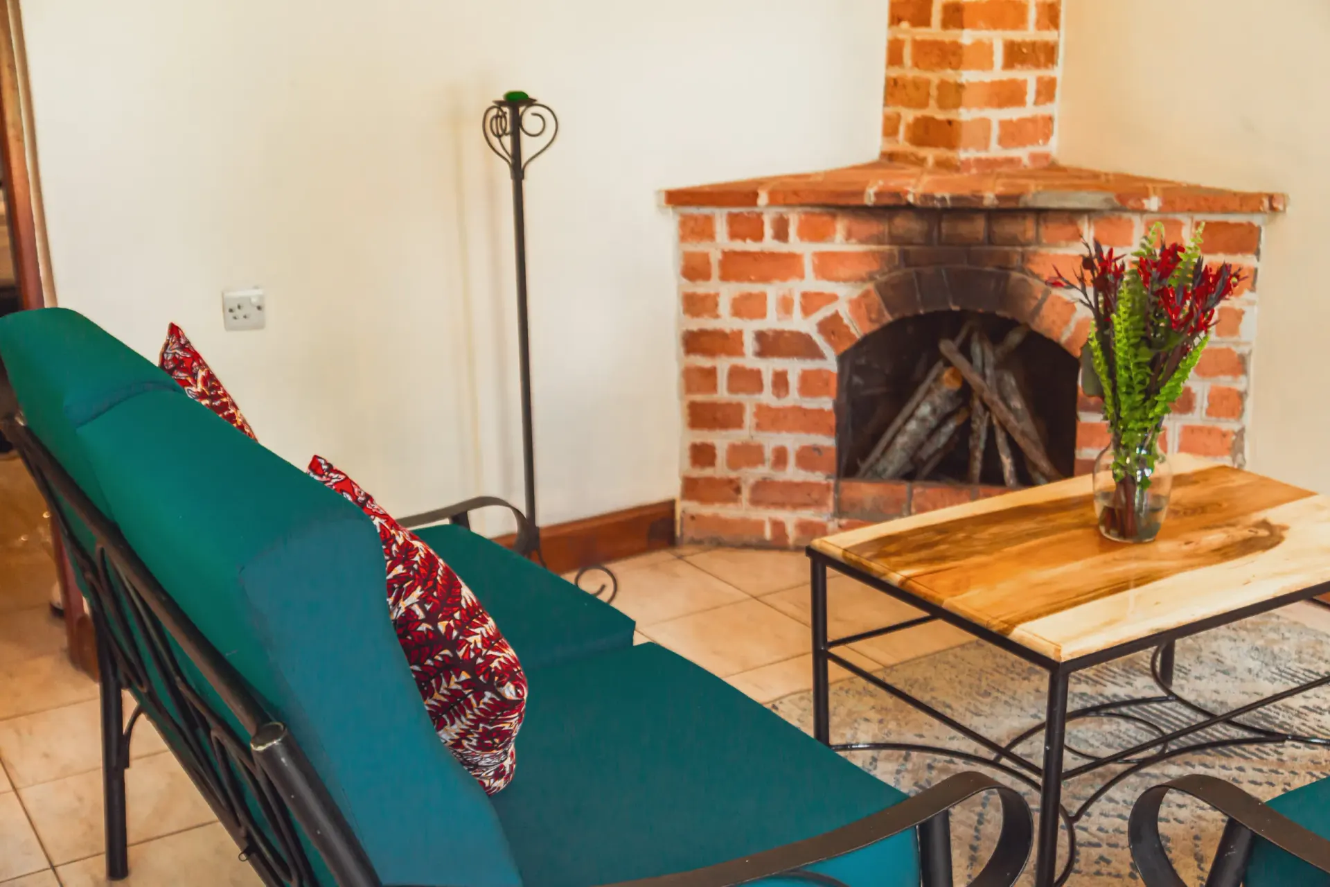 A cottage living room with a brick fireplace, a teal sofa with kitenge cushions and a wooden coffee table