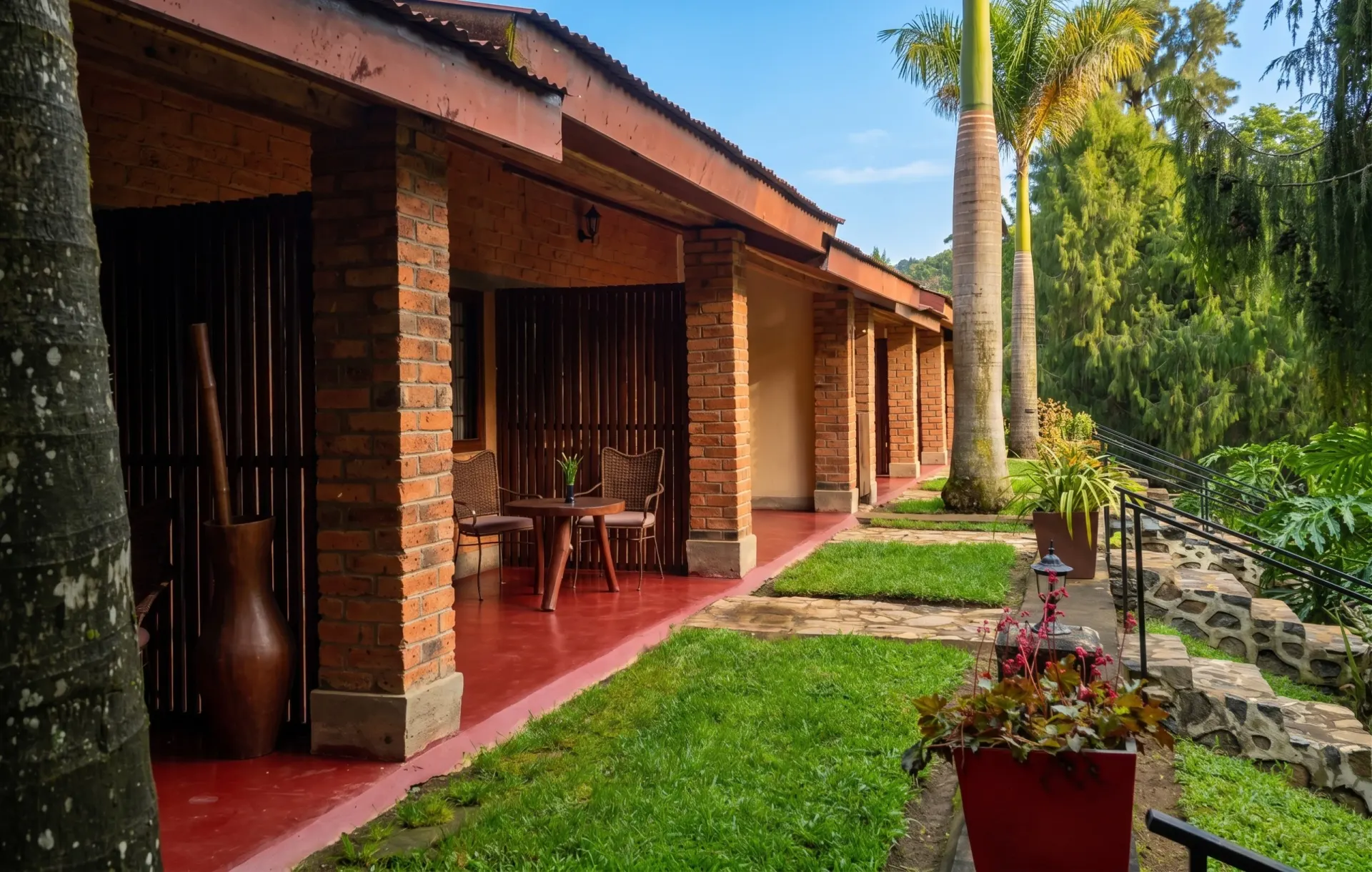 The brick guest cottages along a covered veranda, a tall palm rising beside the red-floored walkway